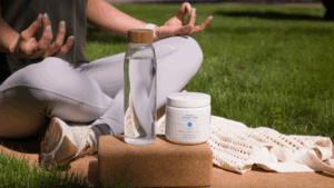 Woman doing yoga in the grass with water and Creatine.
